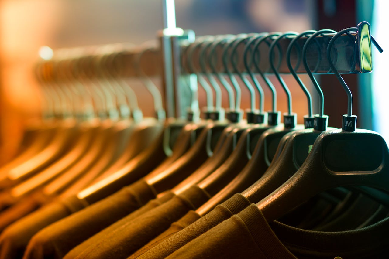 get-in-touch A row of neatly arranged clothes hanging on a rack with wooden hangers.