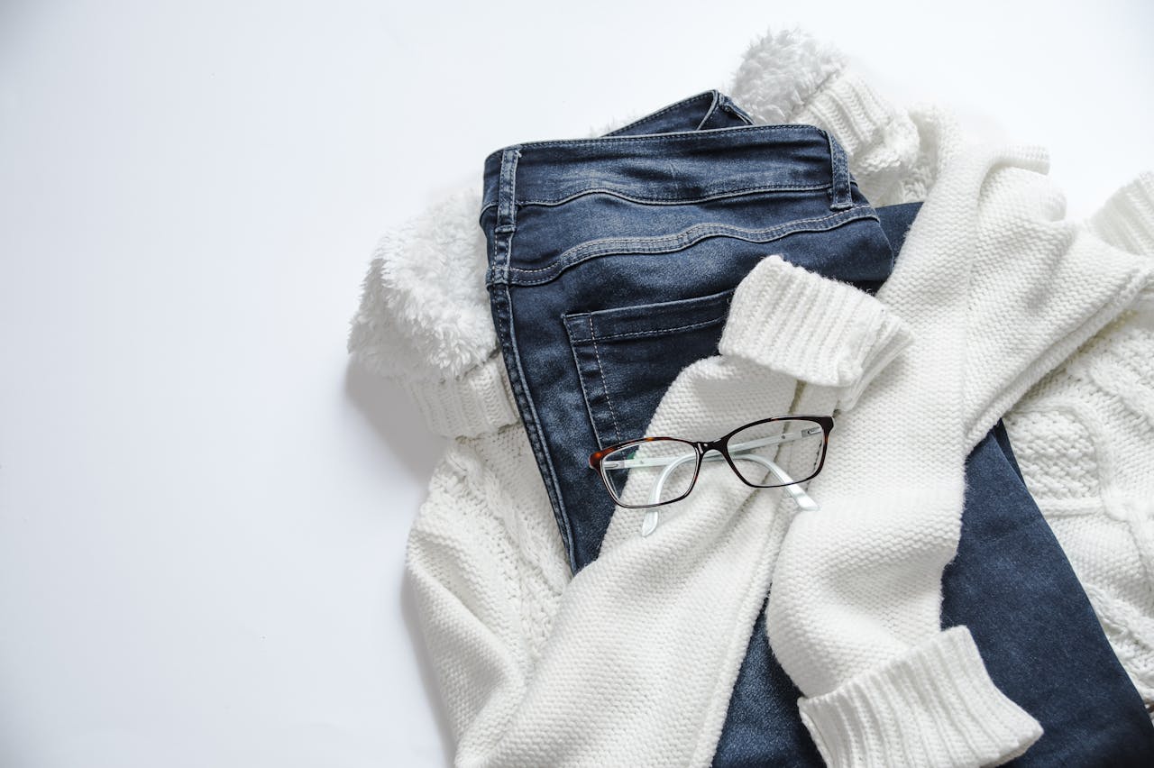 services-05 Stylish flat lay featuring denim jeans, white sweater, and eyeglasses on a bright background.